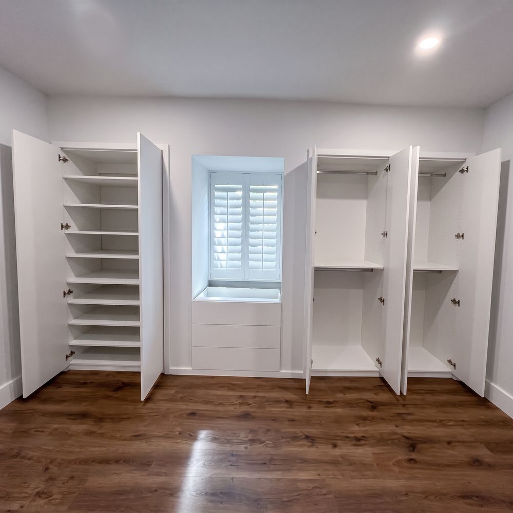 Closet blanco a la medida con torres de zapateras y puertas abiertas sobre piso de madera oscura