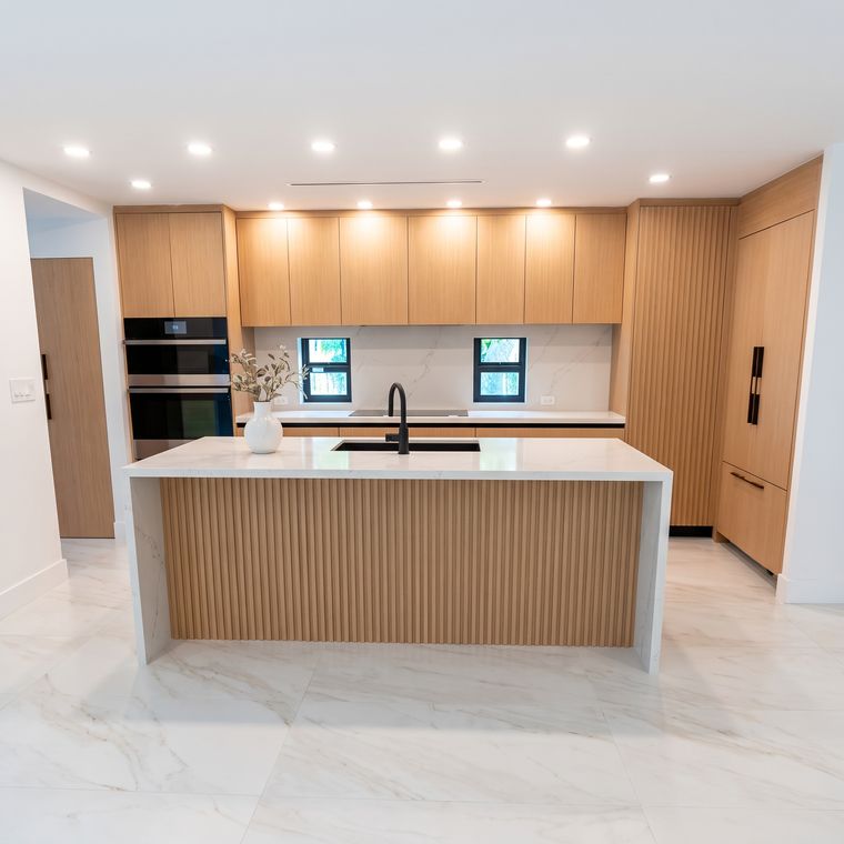 Cocina abierta en madera clara con isla de mármol y torre de hornos