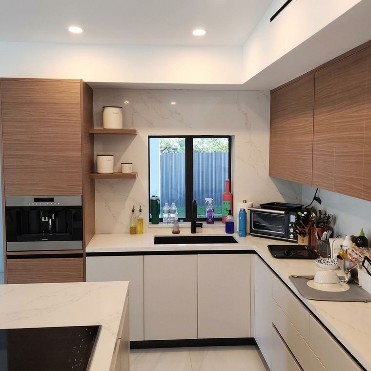 Cocina en U con gabinetes blancos y superiores de madera junto a ventana
