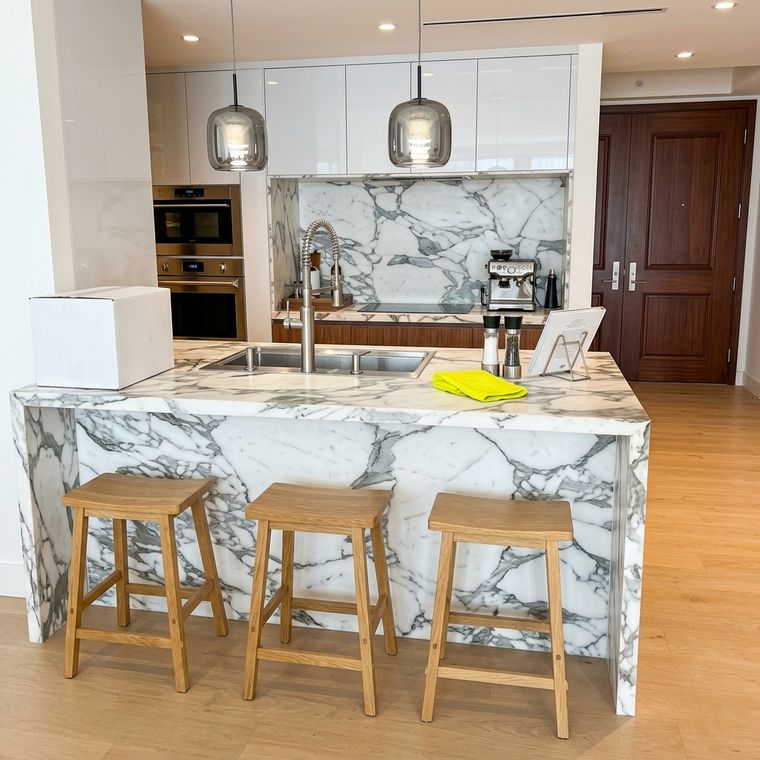 Isla de cocina con cascada de mármol veteado y banquetas de madera