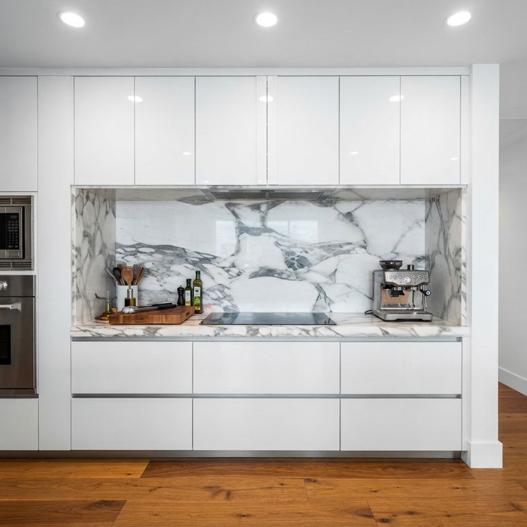 Frente de cocina blanco con backsplash de mármol y hornos empotrados